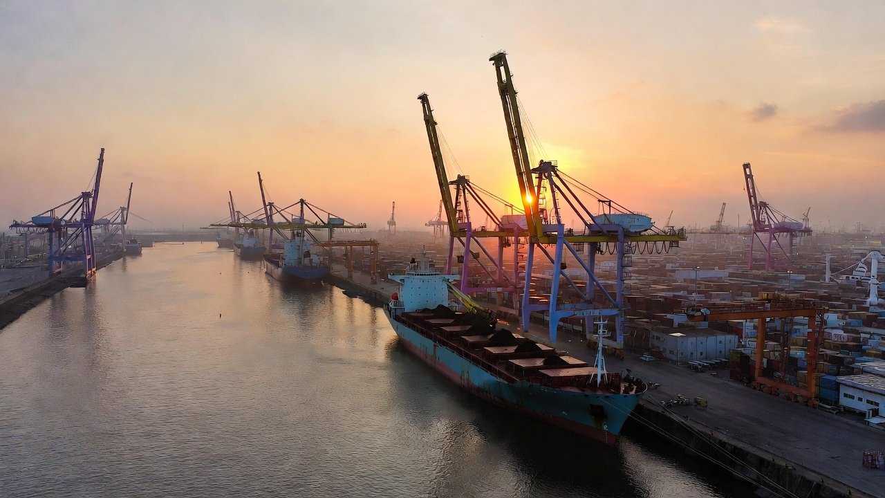 Vista aérea de un gran puerto comercial al atardecer, con buques de carga, grúas pórtico y contenedores en operación en el Caribe colombiano.